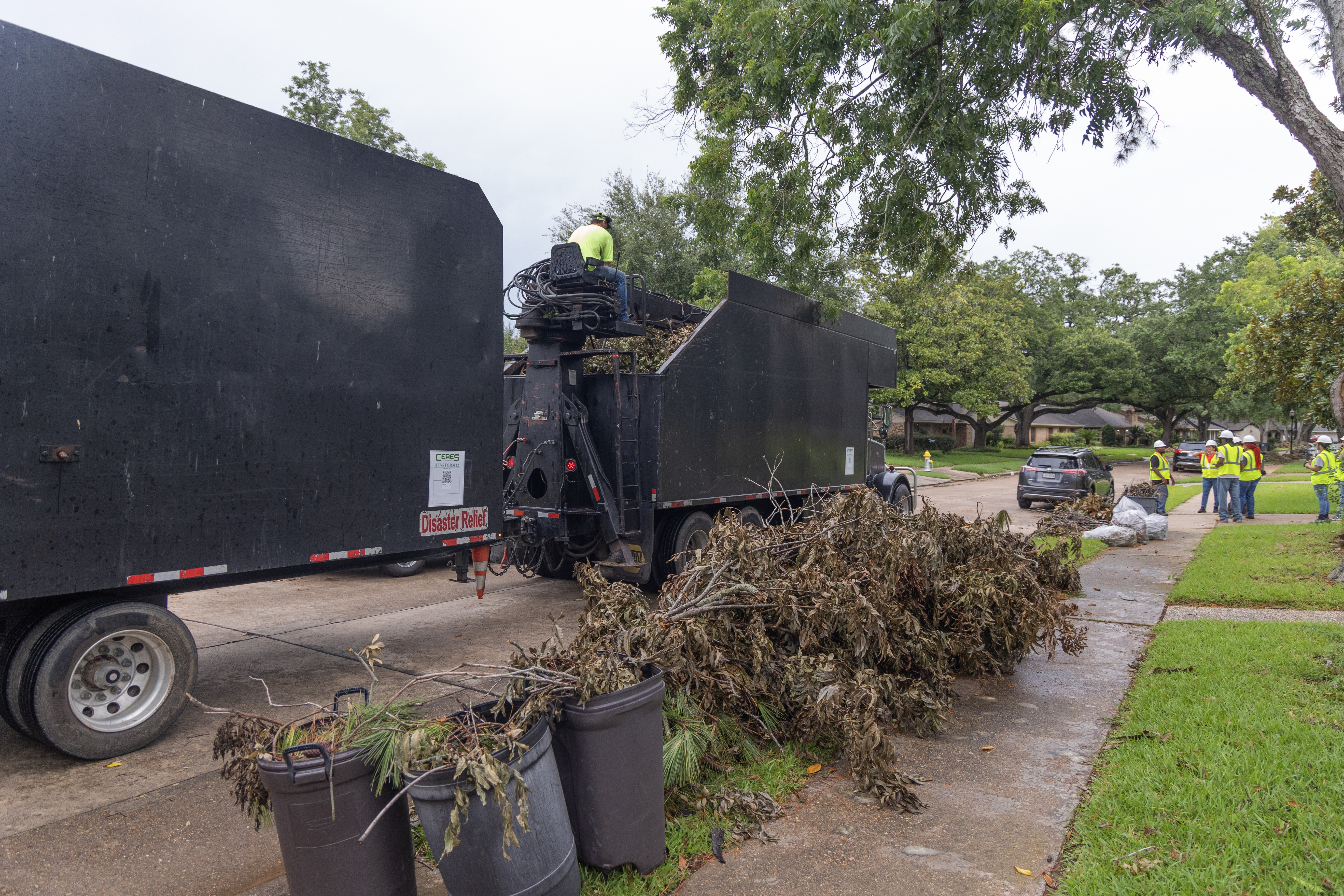 Large debris removal truck picking up piles of tree limbs after a hurricane.